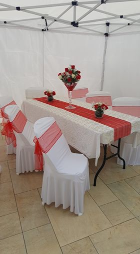 Housse de chaise universelle et noeud de chaise en organza rouge placé devant une nappe blanche pour une cérémonie de mariage